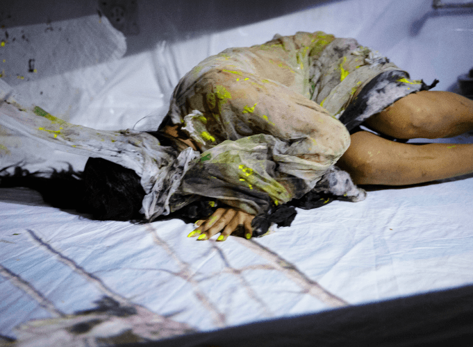 Sofi lies on the ground with fabric on her with green stain marks. projection is on top of the dancer on the ground