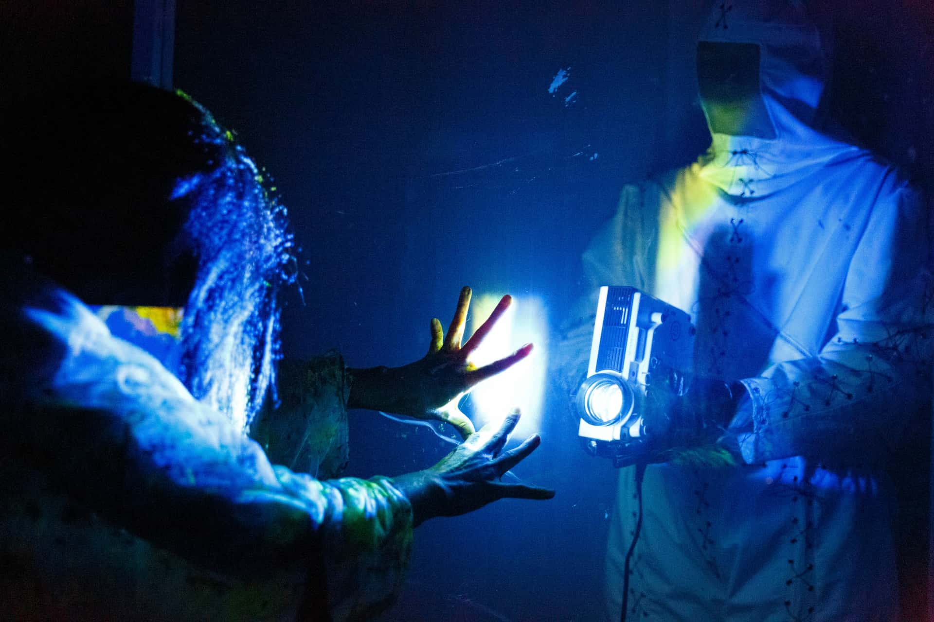 La Llorona is under surveilance by a person in hazmat suit who shines a bright light onto her from behind a glass wall